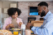 © wavebreak3 - African american couple sitting at dining table cutting breakfast food, sipping orange juice
