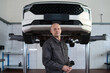 © pressmaster - Portrait of middle aged Caucasian man standing in auto repair shop under elevated car, holding gloves and looking at camera, representing professional mechanic at workplace