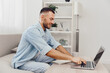 © SHOTPRIME STUDIO - Smiling man working on laptop, enjoying a productive moment at home. Bright, cozy interior with plants fosters a relaxed atmosphere for creativity and focus.