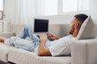 © SHOTPRIME STUDIO - Relaxed man working on a laptop at home, wearing comfortable clothes and sitting on a cozy sofa, embodying the remote working lifestyle trend.