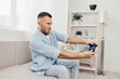 © SHOTPRIME STUDIO - Engaged man enjoying video gaming, showcasing emotion and concentration while playing in a modern, bright living room setting with stylish decor.