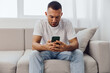 © SHOTPRIME STUDIO - Concentrating man using smartphone while sitting on a comfortable sofa, dressed in casual attire. A moment of modern lifestyle and technology in a bright room.