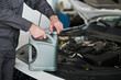 © pressmaster - Unknown man opening motor oil container near car engine, preparing for oil change or vehicle maintenance in automotive workshop, hands and arms visible in close up