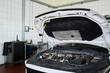 © pressmaster - Car engine compartment exposed with hood open in automotive workshop, showing detailed view of engine components and diagnostic equipment in background, no people visible
