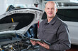 © pressmaster - Portrait of middle aged Caucasian man standing in auto repair shop holding digital tablet, smiling at camera with open car hood in background, demonstrating automotive diagnostics