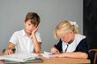 © svetograph - Children Homework Bored Classroom - Two children, a boy and a girl, sit at a table in a classroom, one looking bored while the other does homework.