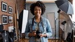 © ArtMajestic - Smiling black woman photographer with afro hair holding camera in studio with lighting equipment. Creative career and artistic profession