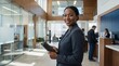 © ArtMajestic - African american woman bank manager holding digital tablet and smiling in modern office lobby. Financial consulting and professional customer service banner with copy space