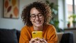 © Abi - Smiling Curly Hair Woman in Orange Shirt Using Mobile Phone Indoors