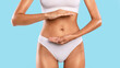 © Prostock-studio - Closeup cropped view of woman holding hands near belly presenting empty free space for product advert, measuring invisible item, female palms making gesture showing big amount or size at blue studio