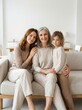 © NataliPro - A grandmother, mother, and daughter sitting together on a sofa, smiling warmly at the camera.