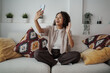 © Friends Stock - Smiling Woman Greets Friends Remotely, Woman From Her Living Room Waves Happily During Video Interaction