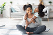 © Prostock-studio - Beautiful black mother and daughter in sportswear cuddling while exercising together at home, cute teen girl hugging her pretty mom sitting on yoga mat, living room interior, copy space