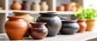© pvl0707 - Handmade clay vases and pots on shelf in pottery studio with blurred ceramic products in background and natural light illuminating workspace