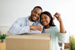 © Prostock-studio - Real estate concept. Loving african american young spouses posing with moving boxes and new house key, hugging and smiling to camera, standing in room full of boxes