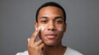 © xuxu - An African American man applies cream to his problematic facial skin, which is suffering from acne. Male skincare and procedures to maintain healthy skin. Daily use of cosmetic products.