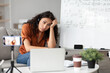 © Prostock-studio - Portrait of shocked and tired female teacher in headset having virtual class, recording online lesson using smartphone on tripod, looking at laptop screen, sitting at table near whiteboard
