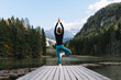 © nataliaderiabina - Mature fit woman practicing yoga on pier by lake overlooking green nature and mountains. Beautiful female in harmony with nature outdoors. Concept of wellbeing, life balance, mindfulness, zen energy.