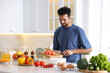 © New Africa - Man adding cut tomatoes into bowl at table in kitchen. Space for text
