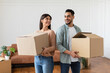 © Prostock-studio - Loving couple carrying cardboard boxes together, standing back to back looking at each other in living room on moving day. Young tenants relocating to new apartment with belongings, unpacking things