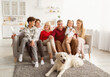 © Prostock-studio - Portrait of big multi generation family with their pet dog sitting on couch, smiling at camera, having fun at home. Cute kids with parents and grandparents spending time together indoors