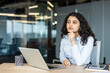 © Liubomir - Young businesswoman with dark curly hair sitting at an office desk with a laptop, deeply engrossed in thought and focused on her professional ambitions and success