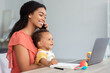 © Prostock-studio - Black Woman Talking On Cellphone And Using Laptop With Baby On Hands, Busy Mother Working Online On Computer While Babysitting Her Toddler Child At Home, Enjoying Remote Job Opportunities, Side View