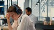 © DC Studio - Stressed programmer in office listening music to relax while working with complex AI calculations. Fatigued IT employee putting audio headphones on, training deep learning systems, camera B