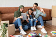 © Prostock-studio - Positive middle eastern family of three having video call with friends or family using tablet in their new home, waving to camera, copy space. People moving to their own apartment, doing repair