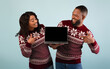 © Prostock-studio - Great discounts and sales for New Year. Excited african american couple showing laptop with blank screen, pointing on it and wearing warm sweater on blue background, studio shot