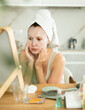 © JackF - Adult woman in towel turban on head applying hydrating face mask during daily self-care routine after shower at home..