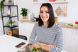 © Xavier Lorenzo - Young happy beautiful woman in a striped shirt smiling at camera with a bowl of salad sitting in the kitchen at home