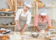 © JackF - Two female bakers working in kitchen, young woman cutting dough into pieces and older woman kneading dough in light bakery