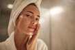 © Boadicea - Woman in bath robe and towel applying skincare product during morning beauty routine in a bathroom