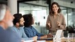 © Nexa - Confident female leader smiling and gesturing while leading a business meeting with a diverse team in a modern office setting.