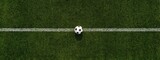 A top-down shot showcases a soccer ball resting on the center line of a grass field, the lines marking the playing area