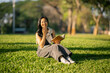 © Wasana - Asian woman smiling reading book in park grass
