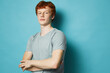 © SHOTPRIME STUDIO - Young redhead man with crossed arms wearing gray t shirt standing confident against blue background looking at camera with relaxed expression portrait