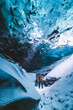© Cavan Images - woman surrounded by blue ice cave walls in glacier in Iceland