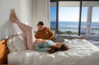 © wavebreak3 - Diverse couple lying on bed supporting baby bump beside sliding glass doors overlooking calm ocean