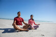 © wavebreak3 - Diverse couple practicing meditation sitting cross-legged on oceanfront beach under clear sky