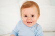 © Any Grant - Baby close-up portrait, smiling and joyful little child on a white bed in a blue bodysuit