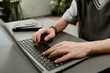 © AnnaStills - Caucasian young adult man typing on laptop at desk, hands visible on keyboard, notebook placed nearby, working or studying in modern indoor setting, focus on technology use