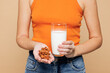 © ViDi Studio - Cropped close up young woman wear orange top casual clothes drink almond milk hold nuts in palm isolated on plain pastel beige background. Proper nutrition healthy fast food unhealthy choice concept.
