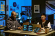 © AnnaStills - Young adult Black man and young adult Caucasian man working on laptops with code visible on screens in modern office at night, focused on programming tasks, another in background