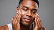 © xuxu - An African American man applies cream to his problematic facial skin, which is suffering from acne. Male skincare and procedures to maintain healthy skin. Daily use of cosmetic products.