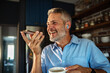 © Geber86 - Smiling middle-aged man using voice command on smartphone in home kitchen