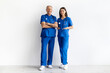 © Anastasiya - Male and female doctors in blue medical uniforms standing together on white background, confident healthcare professionals portrait, copy space