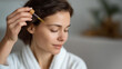 © forenna - A hand gently places a drop of nutrient-rich oil from a pipette onto the scalp in a cozy home spa setting, illustrating personalized care for hair vitality. This approach highlights the benefits of