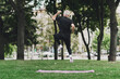 © deagreez - Active senior man leaps in a city park during outdoor workout with a pink mat on the grass for fitness and wellness